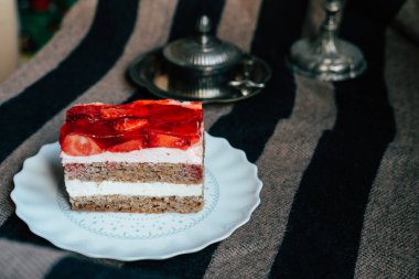 Sıcak çizgili bir masa örtüsünün üzerinde duran lezzetli bir dilim çilekli pastanın tadını çıkar. Pastada krema ve taze çilek katmanları var..