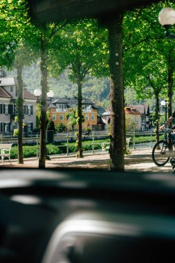 Bir bisikletçi, verimli ağaçlar ve büyüleyici binalarla çevrili Bad Ischl 'deki güzel gezinti alanında sakin bir gezinti yapıyor. Yukarı Avusturya 'daki bu canlı sahneye güneş sıcacık bir ışık saçıyor..