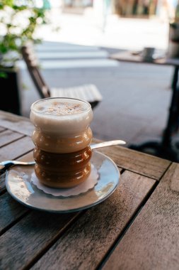 Köpüklü yulaf sütüyle kaplı sıcak bir fincan chai latte basit bir tabakta oturur. Kafenin kırsal ahşap masası güneşli bir günde davetkar atmosferi arttırır..