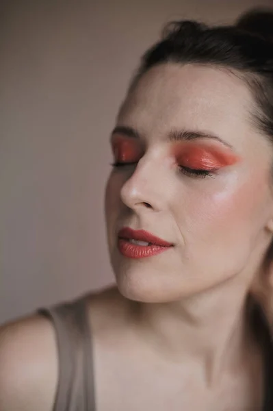 Portrait of a woman with closed eyes wearing extraordinary makeup with red eyeshadows and red lipstick, with her hair tied up