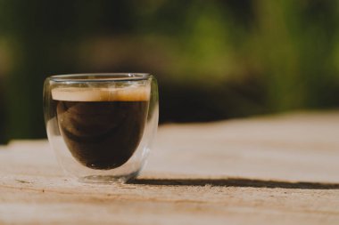 Ahşap bir yüzeyde, arka planda bitki dolu bir havuz olan çift cam espresso bardağı.