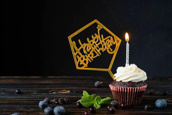 Doğum günü için çikolatalı pasta, mumlar ve yazıtlar, üzümlü üzümlerin yanında ve koyu arkaplanda nane şekeri, metnin altında.