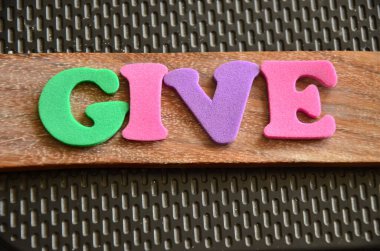 Hayırseverlik kelimesi ahşap arka planda soyut renkli harflerle yazılmıştır.