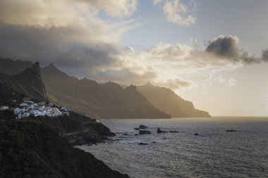 Landscape showing a white walled village clinging to the cliffside as the sun sets clipart