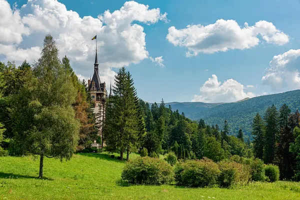Romanya. Peles Castle - Ağustos 2019: Romanya 'daki Peles Kalesi, kısmen yemyeşil ağaçlarla kaplanmış, parçalı bulutlu bir gökyüzüne karşı kurulmuş..
