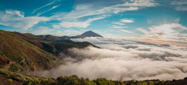 Tenerife 'deki Teide Dağı' nın üstünde bulut tepesi bulutların üstünde yükselen volkanik zirvesiyle parçalı bulutlu mavi gökyüzünün altında.