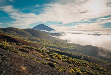 Tenerife 'deki Teide Dağı' nın üstünde bulut tepesi bulutların üstünde yükselen volkanik zirvesiyle parçalı bulutlu mavi gökyüzünün altında.