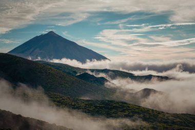 Tenerife 'deki Teide Dağı' nın üstünde bulut tepesi bulutların üstünde yükselen volkanik zirvesiyle parçalı bulutlu mavi gökyüzünün altında.