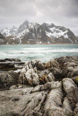 Sakin bir fiyort, karlı dağları ve engebeli kayaları yansıtarak dramatik bir Kuzey Kutbu manzarası oluşturur.