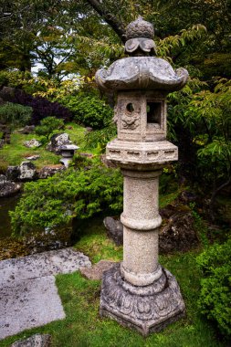 Uzun, yontulmuş bir toro, Japon bahçesindeki yeşil çalıların ve ağaçların arasında duruyor.