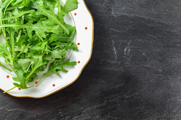 Fresh green arugula or garden rocket leaves on white plate with red dots, black table space for text right side under. Healthy greens and salads concept.