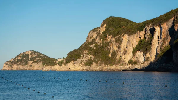 在Liapades湾的岩石悬崖峭壁上 有几棵树 阳光普照 平静的海水和船用浮标在前方 — 图库照片