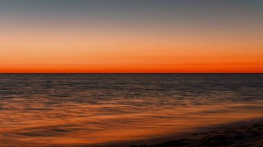 Vibrant orange red sky reflecting in calm ocean after sunset. Minimal landscape photo with space for text.