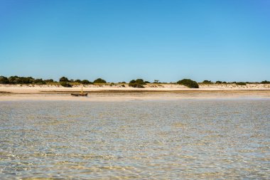 Calm shallow sea on sunny day, fishing boat in distance, sandy shore background, typical landscape at Anakao, Madagascar.