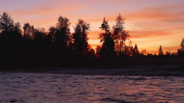 川での夜の風景 夕焼け色の空の背景を持つ岩場の海岸の木々のシルエット — ストック動画