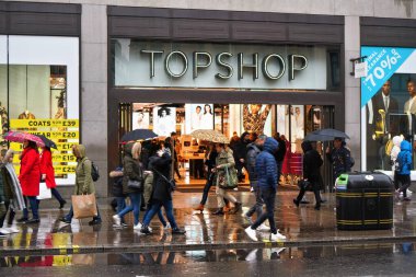 Londra, Birleşik Krallık - 01 Şubat 2019: Londra şehir merkezindeki şubelerinden birinin Topshop mağazası girişindeki ıslak kaldırımda yürüyen yayalar, yağmurlu bir günde şemsiye takıyorlar.