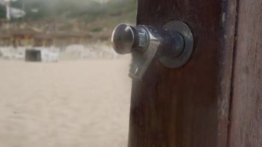 Ahşap sahil duşunda ellerini su altında yıkayan genç bir kadın.