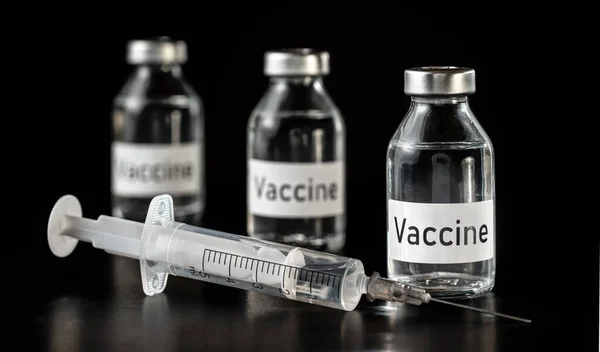 ブラックボード上の3つのガラスワクチンのバイアル 近くの低血圧の注射器 — ストック写真