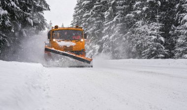 Orange maintenance plough truck on forest road after snowstorm blizzard. Roads get dangerous during winter driver face blurred unrecognizable . clipart