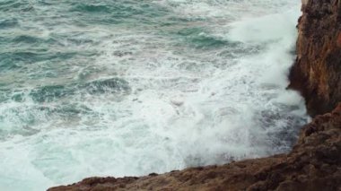 Kayalık kıyıya vuran deniz, sıçrayan yeşil su, yukarıdan görünen beyaz köpük, yavaş çekim videosu
