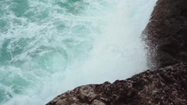 Kayalık kıyıya vuran deniz, sıçrayan yeşil su, yukarıdan görünen beyaz köpük, yavaş çekim videosu