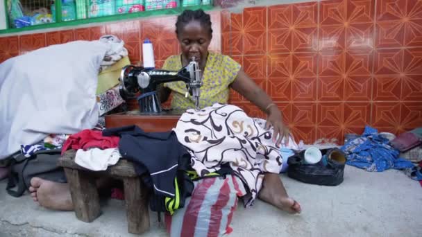 2019年5月1日 马达加斯加托利亚拉 不知名的马达加斯加妇女坐在市场旁边的街上 用手柄缝纫机缝补衣服 更多的人在后台行走 — 图库视频影像
