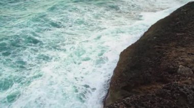 Kayalık kıyıya vuran deniz, sıçrayan yeşil su, yukarıdan görünen beyaz köpük, yavaş çekim videosu