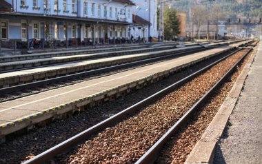 Güneşli bir günde küçük bir şehirdeki tren istasyonu, sığ bir saha fotoğrafı, beton platform ve çelik demiryolu ön planına odaklan