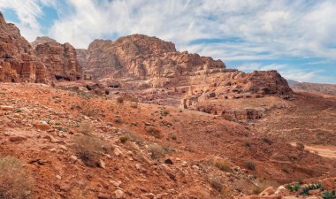 Petra, Ürdün 'deki tipik manzara, kırmızı tozlu zemin, içinde oyulmuş binalar olan dağlar.