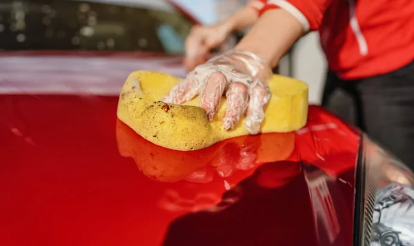 年轻女子洗车前盖 用塑料手套手拿着黄色海绵进行特写 — 图库照片