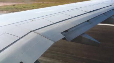 Kalkış sırasında ticari uçak penceresinden bakıldığında, kanatların altında kahverengi gri asfalt görünür.