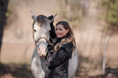 Beyaz Arap atının yanında duran genç bir kadın, kulaklarıyla tutuyor, güneş üzerlerine doğuyor, yakın çekim ayrıntıları.