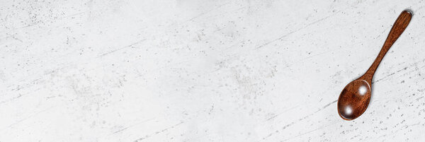 Маленькая ложка из темного дерева, на белой рабочей доске, вид сверху, место для текста слева