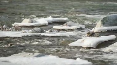 Kış nehri kar ve buzla kaplı taşların yakınından akıyor.
