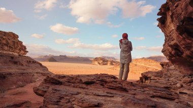 Çöl manzarasında kayalık zeminde duran genç bir kadın, arkadan bakıyor. Wadi Rum, Ürdün