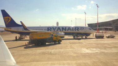 Eilat, İsrail - 23 Ocak 2020: Güneşli bir günde Ryanair uçağını hazırlayan yer personeli, arka planda turuncu yakıt kamyonu, havaalanı terminali binası