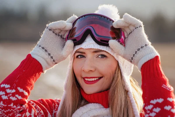 赤い冬のプルオーバーで若い女性 白い帽子 彼女のスキーゴーグルを固定します ぼやけた雪の国の背景 クローズアップの詳細 — ストック写真