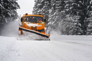 Kar fırtınasından sonra orman yolunda turuncu bakım kamyonu. Yollar kışın tehlikeli olur (sürücü yüzü bulanıklaşır)