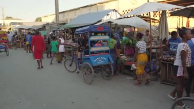 Toliara, Madagaskar - 01 Mayıs 2019: Akşamları tipik orta büyüklükteki bir kasaba caddesinde yürümek, her iki tarafta market tezgahları, Malagasy 'li insanlar yürüyor, bazıları bisiklet sürüyor veya çocuk arabası kullanıyor.