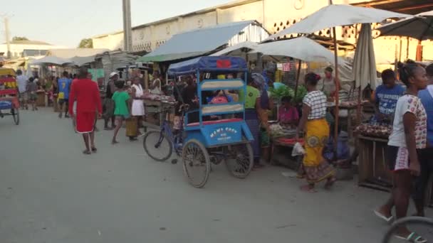 トリアラ マダガスカル 2019年5月1日 夕方に典型的な中規模の町の通りを歩く 両側の市場の屋台 マダガスカル人が歩く いくつかの乗馬自転車やペディカブ人力車 — ストック動画
