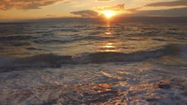 Güneş dramatik günbatımı bulutları arasından parlıyor Ölü Deniz 'in Ürdün tarafında dalgalar, tuzla kaplı kıyıdaki kum