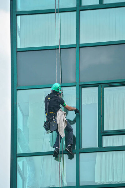 Промышленный мойщик окон - человек, висящий на крышах с защитным оборудованием, очищающий фасад высотного современного стеклянного здания.