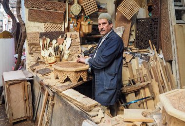 Fez, Fas - 07 Ocak 2020: Bilinmeyen bir adam ahşap işinde çalışıyor veya sokak pazarının yakınında oyma atölyesi işletiyor. Etrafında bir sürü ahşap hediyelik eşya ve ürün vardı.