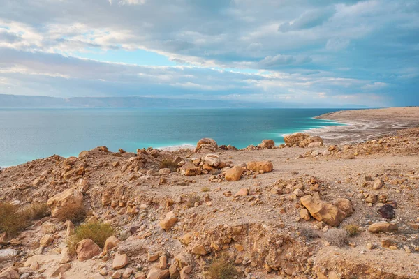 ヨルダン側の死海の海岸 乾燥した砂と岩のビーチ 太陽は美しい紺碧の水面に輝きます — ストック写真