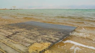 Güneşli bir günde kumsal kıyısı, küçük dalgalı su - Ein Bokek, İsrail 'de ölü deniz tatil köyü