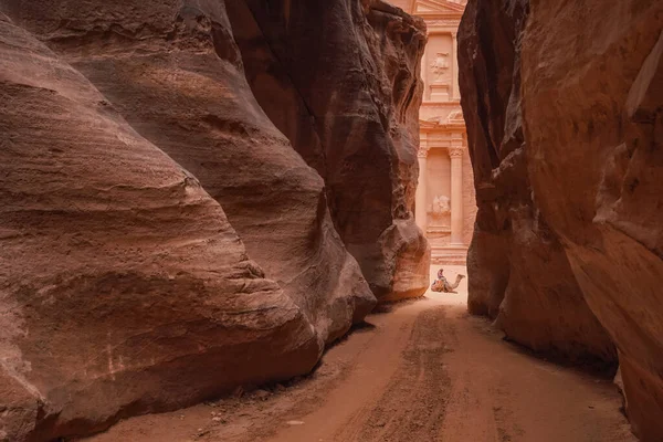 约旦Petra的Al Siq峡谷 两边都是粉红色的红色砂岩墙 坐在骆驼距离上的人难以辨认 身后是宝殿 — 图库照片