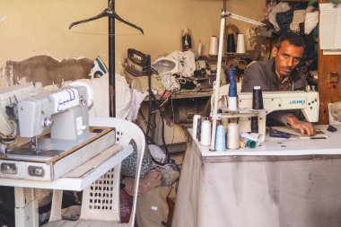 Marakeş, Fas - 02 Ocak 2020: Kimliği belirsiz bir adam dikiş makinesiyle çalışıyor, atölyesinde ve pazarında satılacak giysileri onarıyor