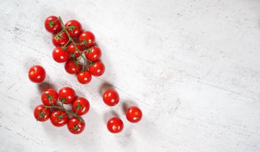 Vibrant small red tomatoes with green vines on white stone like board, view from above, empty space for text right side