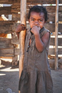 Ilakaka, Madagaskar - 30 Nisan 2019: Sokakta tahta barakanın yanında duran, turistler tarafından bağışlanmış giysiler giyen, fakir görünümlü çocuk