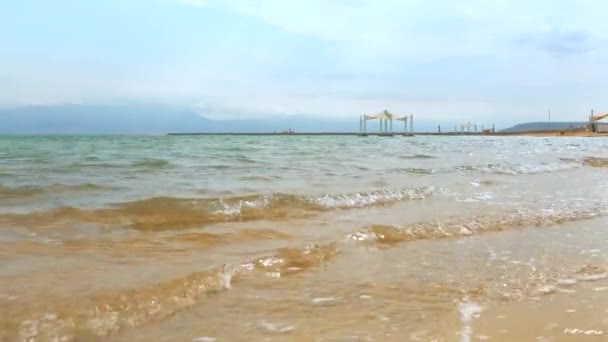 Ein Bokekで穏やかな一日死海のビーチ 青い緑色の水 近くの太陽の日陰の避難所 太陽は砂浜の海岸に輝いています — ストック動画